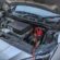 A car's hood is raised, and a battery is positioned on the ground nearby.