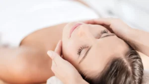 Woman relaxing with eyes closed as a therapist's hands massage her temples during a facial at St. Somewhere Spa