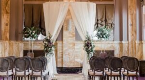 Wedding ceremony setup with a draped floral arch in Sentinel Hotel's Renaissance Room, featuring gold marble walls and period arches in downtown Portland