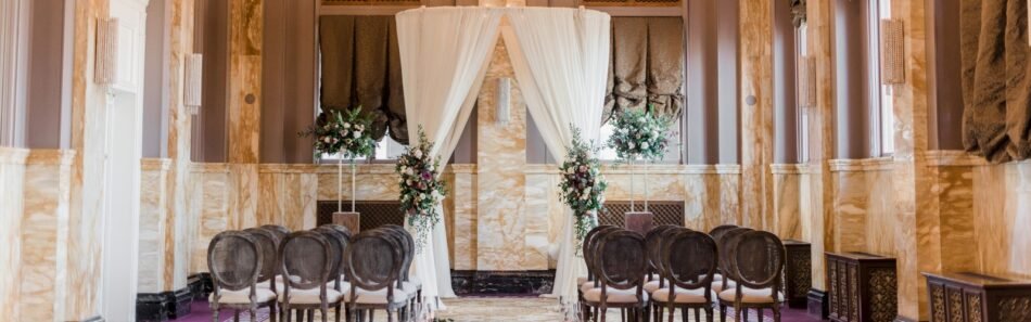 Wedding ceremony setup with a draped floral arch in Sentinel Hotel's Renaissance Room, featuring gold marble walls and period arches in downtown Portland