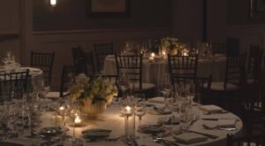 Candlelit round reception tables with white linens, floral centerpieces and dark Chiavari-style chairs at Hotel Viking, a wedding venue in Newport, RI