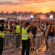 Security staff in hi-vis vests guide festival crowds through entry gates at sunset